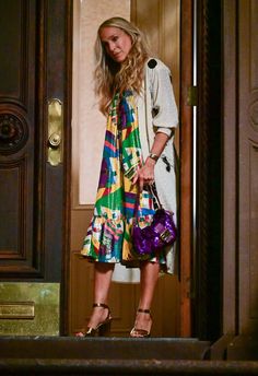 a woman standing in front of a door holding a purple purse and looking at the camera