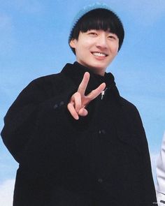 a young man making the peace sign with his hand while standing in front of a blue sky