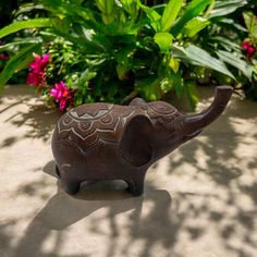 an elephant figurine sitting on top of a cement ground next to plants and flowers