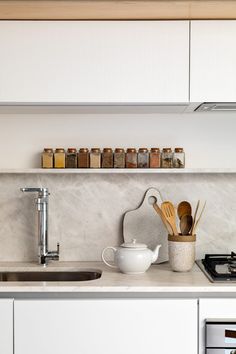 a kitchen with white cabinets and countertops has utensils on the shelf above the sink