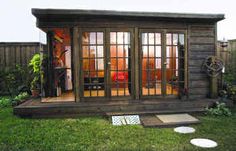 a small wooden shed with glass doors and windows on the outside, in a backyard