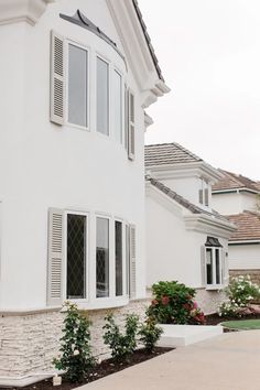 a house with white shutters and flowers in the front yard, on a cloudy day