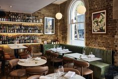 the interior of a restaurant with tables, chairs and wine bottles on the wall behind them