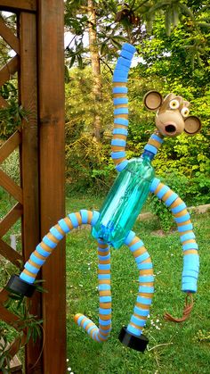 a monkey statue made out of plastic bottles in the grass next to a wooden fence