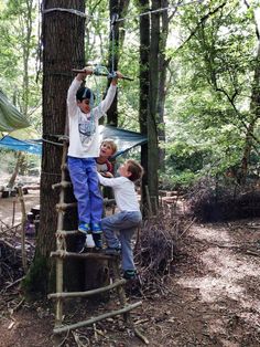 two boys are climbing up a ladder in the woods