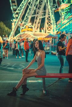 a woman sitting on a bench in front of an amusement park at night with ferris wheel in the background