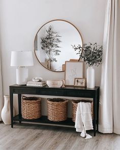 a black console table with two baskets and a round mirror above it on the wall