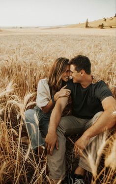 a man and woman sitting in the middle of a wheat field with their arms around each other