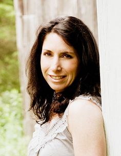 a woman with long dark hair smiling at the camera while standing in front of a fence