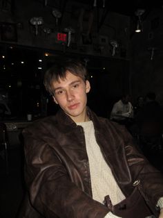 a young man in a leather jacket sitting at a table with his hand on the purse