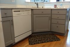 a kitchen with gray cabinets and white appliances in the corner, along with a rug on the floor