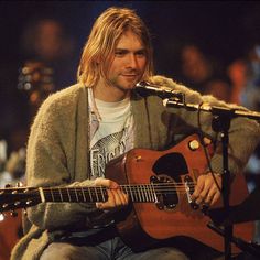 a man sitting in front of a microphone while holding a guitar