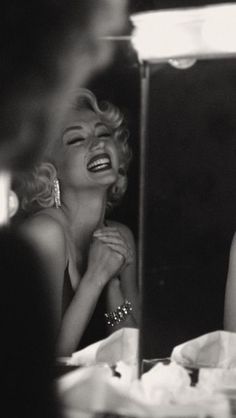 marilyn monroe laughing in front of a mirror while looking at her reflection on the table