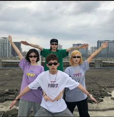 four people posing for a photo in front of a cityscape with their arms outstretched