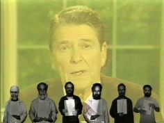 a group of men standing next to each other in front of a screen with a man's face on it