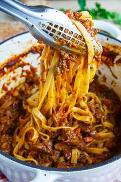 spaghetti being cooked in a skillet with a ladle full of sauce and meat