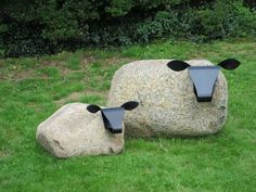 two black sculptures sitting on top of a green field next to a large rock in the grass