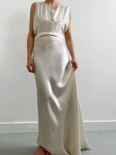 a woman in a white dress is standing against a wall with her hands on her hips