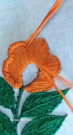 an orange flower is being stitched onto a white cloth with green leaves on it