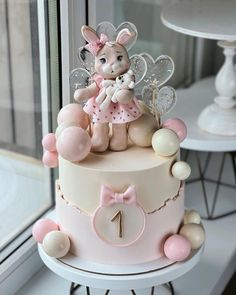 a pink and white cake with a bunny on top sitting in front of a window