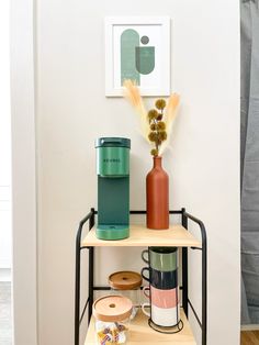 a shelf with coffee cups and vases on it next to a wall mounted art piece