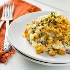 a white plate topped with mashed potatoes covered in sauce and garnished with herbs