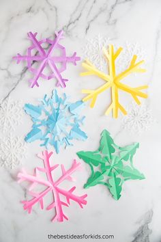 four snowflakes made out of colored paper on a marble surface