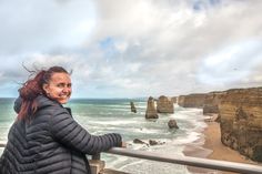 a woman standing on top of a metal railing next to the ocean with cliffs in the background