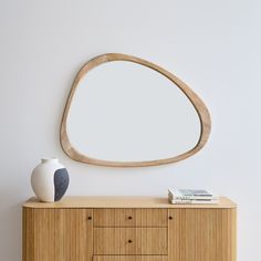 an oval mirror on the wall next to a dresser with two balls and a vase