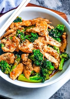 chicken and broccoli stir fry with chopsticks in a white bowl on a wooden table