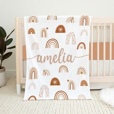 a baby's name blanket with rainbows and clouds on it, next to a crib