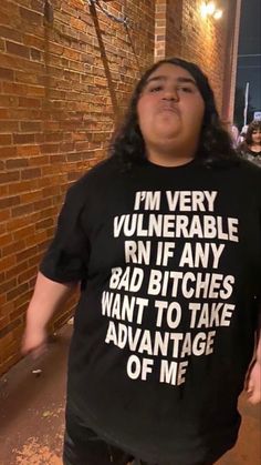 a man standing in front of a brick wall wearing a t - shirt with words on it