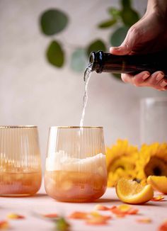 someone pouring wine into two glasses with orange slices and sunflowers in the background