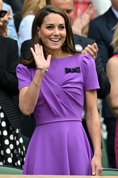 a woman in a purple dress waves to the crowd