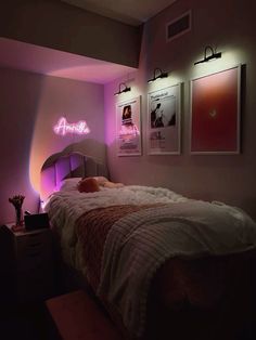 a bed in a room with pink lights on the wall and pictures above it that are lit up