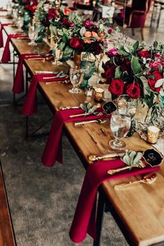 a long table is set with red and green flowers, wine glasses, and candles