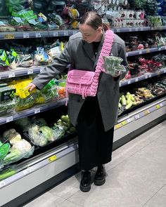 a woman in a grocery store holding a pink basket and looking at the food on display