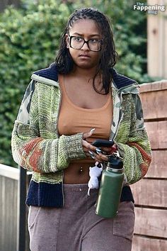 a woman with glasses is holding a cellphone and looking at her phone while walking down the street