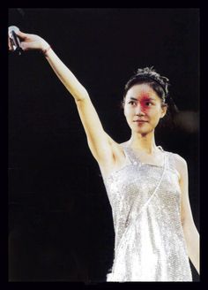 a woman holding up a cell phone in her right hand and wearing a silver dress