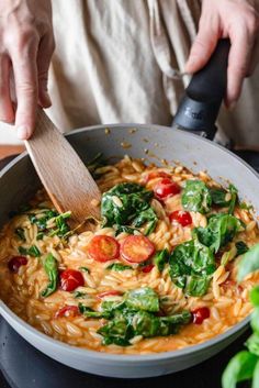 someone cooking pasta with spinach and tomatoes in a pan