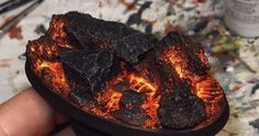 a hand holding a piece of wood that has been lit up with fire and coal