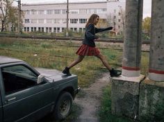 a woman in a skirt is walking on the tracks near a car and train tracks