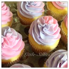 cupcakes with pink and purple frosting sitting in a glass tray on top of a table