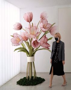 a woman standing next to a vase with pink flowers