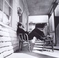 black and white photograph of a man sitting in a chair on the porch with his legs crossed