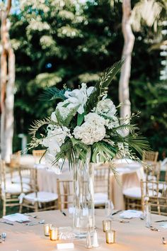 a vase filled with white flowers sitting on top of a table next to gold chairs