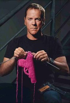 a man is holding a pink crocheted object in his hands and knitting it