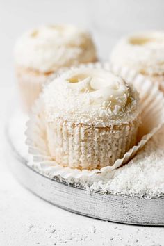 two cupcakes with white frosting sitting on top of a cake plate covered in powdered sugar