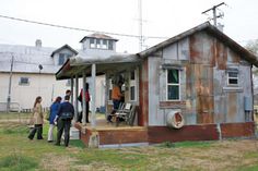 several people are standing outside of an old house that has been turned into a mobile home