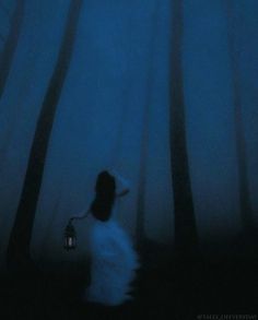 a woman standing in the woods holding a lantern